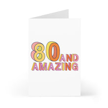 Load image into Gallery viewer, Celebrate with the 80th Birthday Card from R is for Robo, a humorous milestone card for him or her. It features "80 and Amazing" in bold, multicolored letters on a crisp white background. The card stands open, ready for your hand-written note to enhance its festive design.