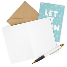 Load image into Gallery viewer, A blank open card with a brown envelope, the "Let it Snow Ho Sassy Christmas Card" by R is for Robo featuring a teal snowy design, and a white pen with gold accents are arranged on a white surface—perfect for crafting your own Merry Christmas messages or sending cheeky holiday greetings.