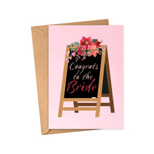 Load image into Gallery viewer, A delightful card by R is for Robo, the "Cute Bridal Shower Card or Engagement Card for the Bride to Be," displays an easel with a blackboard elegantly inscribed with "Congrats to the Bride" in white and pink letters. This charming card is adorned with a bouquet of red and pink flowers and rests on a brown envelope against a soft pink background.