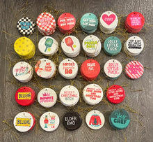 Load image into Gallery viewer, A variety of vibrant, round decorative pieces from R is for Robo, featuring the Oops Seconds Christmas Ornaments collection. These ceramic holiday ornaments display festive or humorous text in many colors, each equipped with a gold string for hanging. Their slight imperfections add a unique charm to your seasonal decor.