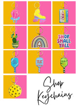Load image into Gallery viewer, Displayed against a vibrant pink and yellow grid background is a lively assortment of colorful keychains. The designs feature a geometric panda, roller skate, vintage cassette, Cactus Gold Enamel, rainbow, amusing phrases, and the charming "Shop Small Y'all" text. Embrace your love for greenery with the Plant Mom Keychain from R is for Robo. Don't miss the "Shop Keychains" message at the bottom to explore more unique offerings.