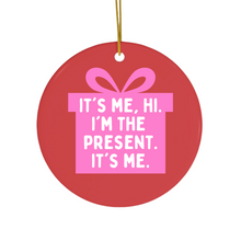 Load image into Gallery viewer, The Pop Culture Gifts Pink Ornament for Girls by R is for Robo is a round ceramic decoration showcasing an illustration of a pink gift box. It features the text, "It's me, hi. I'm the present. It's me." Complete with a gold string for hanging, this distinctive Christmas gift will bring charm to any tree.