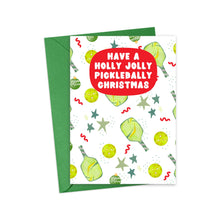 Load image into Gallery viewer, Introducing the Pickleball Christmas Card by R is for Robo—an ideal gift for pickleball enthusiasts! This festive card features green pickleball paddles and balls, adorned with stars and ornaments, all set against a vibrant green envelope. The cheerful red speech bubble on the front reads, "Have a Holly Jolly Pickleball-y Christmas," making it perfect for those looking to give funny pickleball-themed gifts this holiday season.
