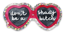 Load image into Gallery viewer, Introducing the **Red Heart Sunglasses Don't Be A Shady Bitch - Funny Sassy Glitter Sticker** by **R is for Robo**. This playful sticker showcases red heart-shaped sunglasses with dark lenses. The left lens bears the phrase "don't be a" and the right lens completes it with "shady bitch," both in elegant white cursive. Enhanced with a glitter shimmer, these striking glasses bring an extra sparkle to your style.