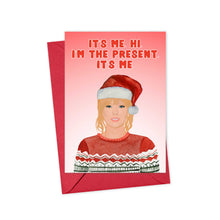 Load image into Gallery viewer, Illustration of a person sporting a Santa hat and festive sweater against a pink background. Text reads, "It's me. Hi. I'm the present. It's me." This amusing holiday card, styled in the spirit of Taylor Swift, is known as the Taylor Swift Christmas Card for Swifties by R is for Robo and comes with a festive red envelope—an excellent choice for spreading cheer this holiday season.
