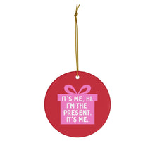 Load image into Gallery viewer, The Pop Culture Gifts Pink Ornament for Girls by R is for Robo features a red ceramic design with a pink gift box topped with a bow. The text on the ornament reads, "It's me, hi. I'm the present. It's me." This charming Christmas decoration hangs elegantly from a golden string.