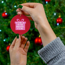 Load image into Gallery viewer, With green nail polish adorning their fingers, an individual displays the unique Pop Culture Gifts Pink Ornament for Girls from R is for Robo in front of a Christmas tree. The ceramic ornament is embellished with a gift icon and the phrase "It's me, hi. I'm the present. It's me." In the background, red baubles are suspended on the tree, enhancing a festive atmosphere filled with holiday cheer.