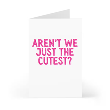 Load image into Gallery viewer, A white greeting card from R is for Robo stands upright, featuring bold pink text on the front that reads, "AREN'T WE JUST THE CUTEST?" It's the perfect funny Valentine's Day card for him or her.