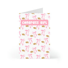 Load image into Gallery viewer, The Funny Graduation Card for Women with Pink Bows Coquette from R is for Robo stands upright, featuring pink bows and gold caps on a white background, with bold pink letters at the top declaring, Congrats, girl!.