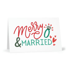 Load image into Gallery viewer, The Merry and Married Christmas Card, a product of R is for Robo, showcases the phrase "Merry & Married" in vibrant red and green letters. The card is adorned with a stylized ring graphic dotting the "i" in Married, and features small red hearts accentuating the bottom right corner, providing an ideal space for a heartfelt handwritten note.