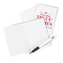 Load image into Gallery viewer, A Tig Ol' Bitties Valentine's Day Card for Wife by R is for Robo, featuring the cover message "I love your tic ol bities," adorned with heart and arrow graphics in red and blue text. An envelope accompanies the card, while a pen on a white surface awaits a heartfelt handwritten note.