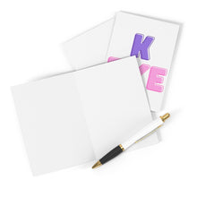 Load image into Gallery viewer, The "K Bye Funny Going Away Card for Coworker or Friend" by R is for Robo rests on an envelope, with part of a decorative card beneath it, showing the letter K in purple and E in pink. Nearby, a pen with a gold clip awaits heartfelt messages or witty goodbyes.
