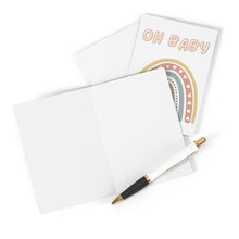 Load image into Gallery viewer, An "Oh Baby Boho Rainbow New Baby Card" from R is for Robo, showcasing a charming boho rainbow and the words "Oh Baby," is propped open beside a white pen with gold accents, perfect for your handwritten message. The simple white background enhances the card’s playful design.