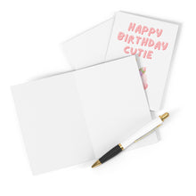 Load image into Gallery viewer, A blank greeting card rests on a white surface with a pen beside it, inviting your personal touch. Behind it, the R is for Robo Kids Birthday Card displays "Happy Birthday Cutie" in pink letters alongside cheerful balloons, making an ideal match for the Cutie Cupcake Birthday Card for Kids theme.