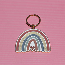 Load image into Gallery viewer, The Boho Rainbow Love Keychain by R is for Robo is a charming metal gold keychain showcasing a stylized rainbow in muted pink, white, and gray hues. The word "LOVE" is gracefully presented on a small heart at the base, set against a textured pink backdrop.