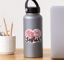 Load image into Gallery viewer, A gray water bottle with a black handle sits on a desk, adorned with an "It's My Turn to Take a Selfish Alexis Sticker" by R is for Robo in pink and black. Nearby are a white textured container of pencils and a white surface partially visible in the background.