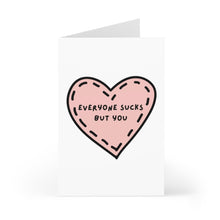 Load image into Gallery viewer, The Everyone Sucks But You Funny Anniversary Card by R is for Robo showcases a pink heart adorned with black stitching lines on the cover. Inside, the message reads, "Everyone sucks but you." Made from heavyweight matte card stock, it stands open against a white background, prepared to brighten your loved one's day.