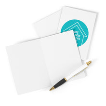 Load image into Gallery viewer, An elegant greeting card from R is for Robo's "Creepers Funny Housewarming Card" collection lies open, complemented by a sophisticated black and gold pen. The card showcases a partially visible teal circular design with an inspiring message ideal for celebrating new beginnings in a new home. Behind it, another card awaits your heartfelt handwritten note.