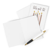 Load image into Gallery viewer, A colorful "Get Lit" Funny Birthday Card by R is for Robo, adorned with candle illustrations, is displayed next to a blank unfolded card, ideal for personalizing with a heartfelt handwritten note. This ensemble is complemented by a sophisticated black and gold pen, all gracefully presented on an immaculate white surface.