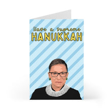 Load image into Gallery viewer, This greeting card, named the RBG Ruth Bader Ginsburg Hanukkah Card from R is for Robo, showcases an illustration of a person sporting glasses and a lace collar on a blue diagonal-striped background. The card features the message "Have a supreme Hanukkah" in bold yellow and white letters, printed on heavyweight matte cardstock.