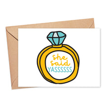 Load image into Gallery viewer, A vibrant engagement card from R is for Robo, featuring the "She Said Yas Funny Engagement Card," showcases an illustration of a large diamond ring with bold yellow and teal text exclaiming "She said YASSSSSS." It comes paired with a brown envelope, ideal for adding your heartfelt handwritten note.
